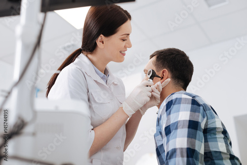 Profile photo of otolaryngologist holding otoscope near ear of patient