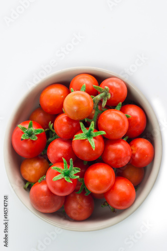 Fresh cherry tomatoes are in a cup on a white background.