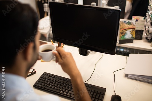 Businessman holding coffee cup by desktop pc in office