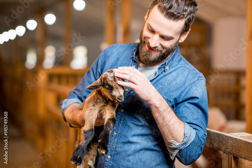 Handsome farmer taking care of cute goat baby at the barn