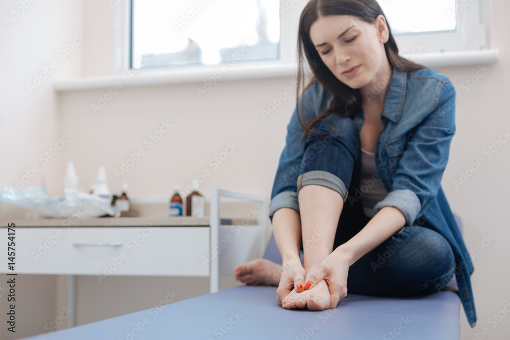 Cheerless moody woman holding her feet Cheerless moody woman holding her feet