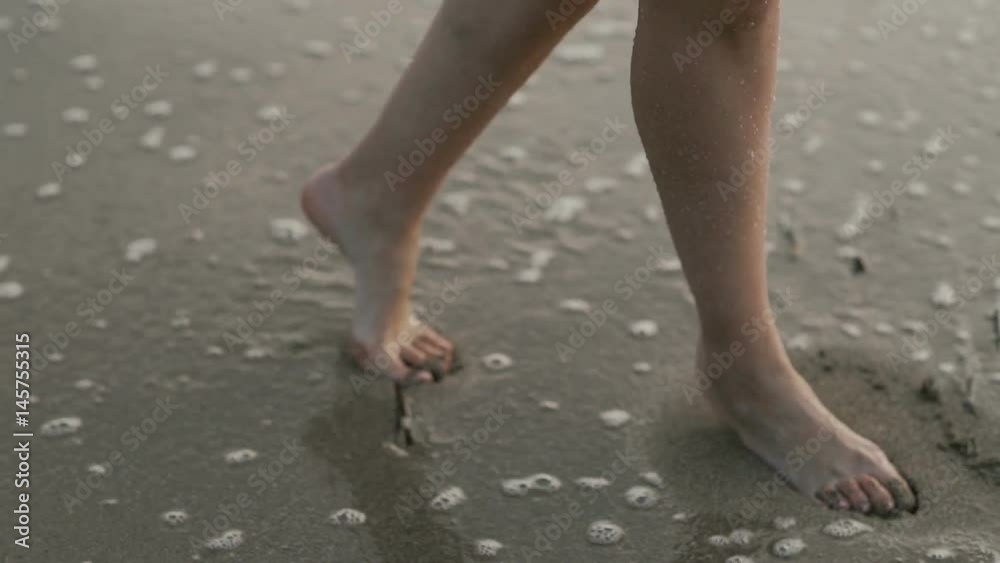 Female feet walk on wet sand on the coast of the sea Female feet walk on wet sand on the coast of the sea