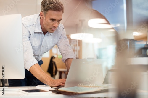 Businessman working on laptop while leaning at desk