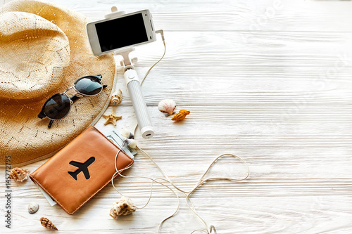 summer travel vacation concept, space for text. selfie stick phone camera passport money plane hat and sunglasses on white wooden background. hello summer. wanderlust. save moments