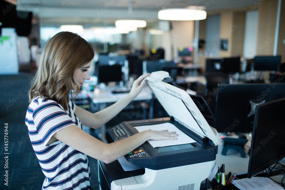 Businesswoman using copy machine in office - obrazy, fototapety, plakaty 