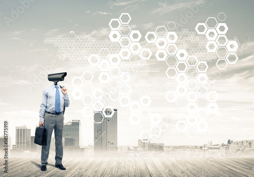 Camera headed man standing on wooden floor against modern citysc photo