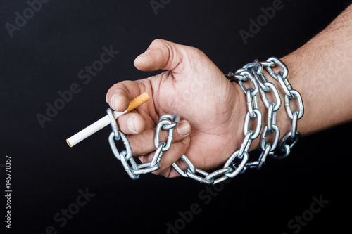 Cigarettes and hand of a man tangled in chains . The concept of nicotine addiction.