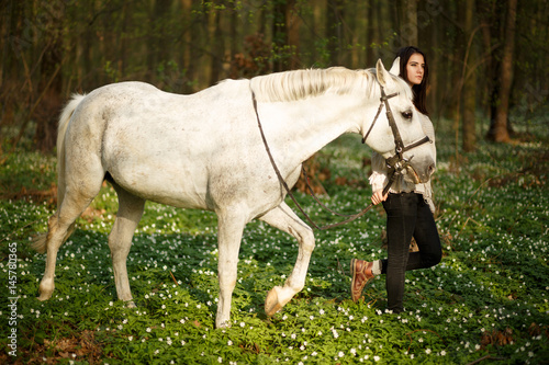 Young beautiful woman with a horse. Female rider and horse in the spring forest. Woman in boho style. © Serhii