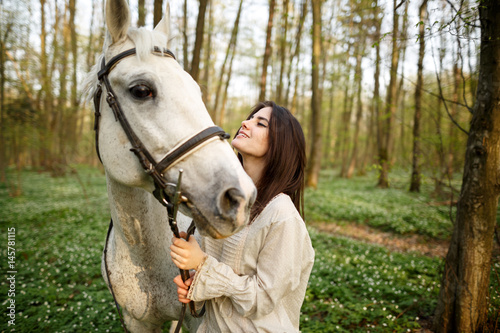 Young beautiful woman with a horse. Female rider and horse in the spring forest. Woman in boho style.