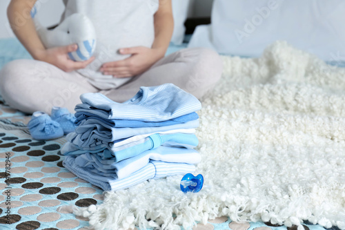 Pile of baby clothes and pregnant woman on bed photo
