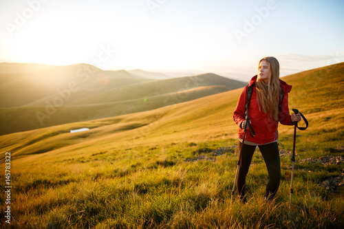 Young woman hiker hiking on mountain trail. Travel concept with space for text. Happy traveler with backpack standing on top of a mountain and enjoying sunset view
