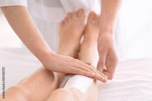 Beautician waxing female legs in spa center