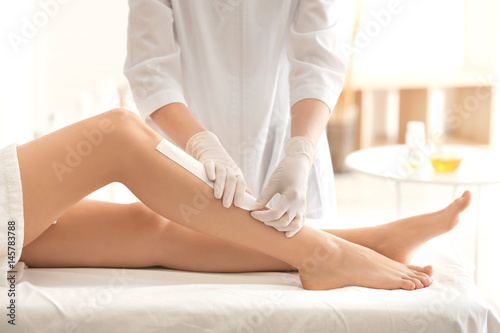 Beautician waxing female legs in spa center