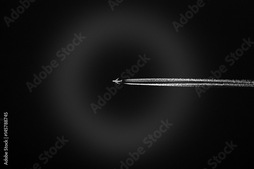 High flying jet with three jet trails lit up white against a dark black sky, atmospheric ring