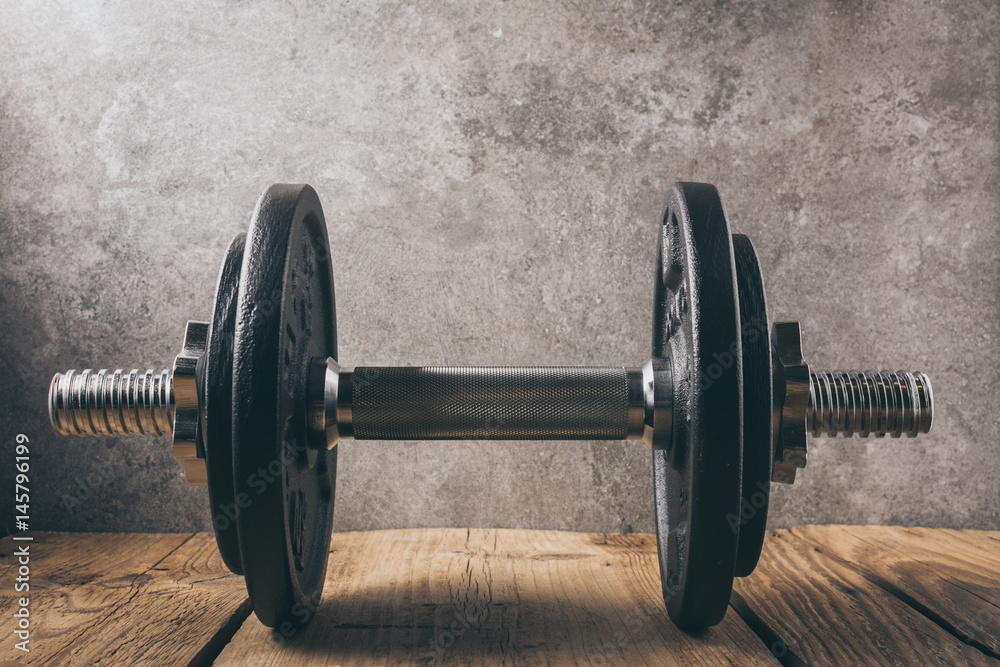 Naklejka premium iron dumbbell on a wooden plank with gray background