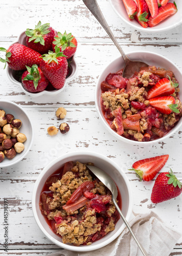 Homemade strawberry and rhubarb crumble  served with fresh berries on light wooden background; Overhead shot