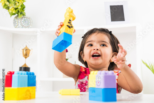 cute indian girl child busy playing with toys or blocks, sitting at table