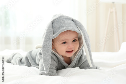 Cute little baby in bunny costume lying on bed at home