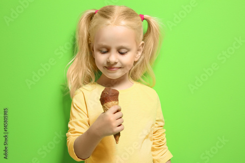 Cute little girl eating ice cream on color background © Africa Studio