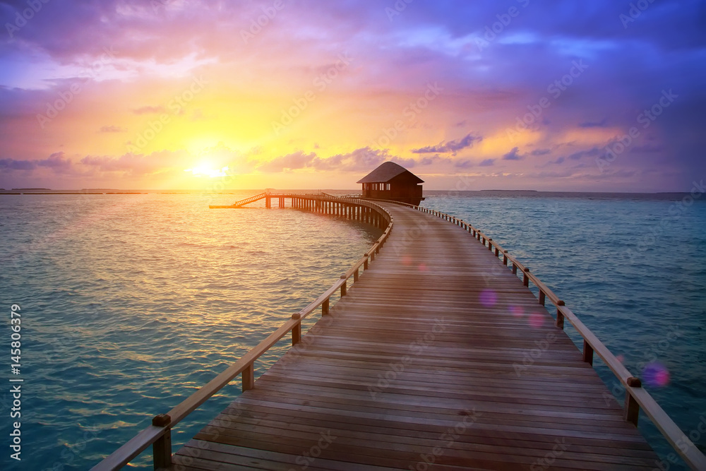 wooden road from the island to a hut over water on a sunset. Maldives...
