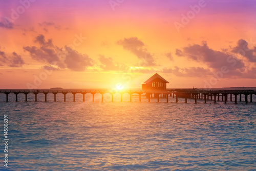 wooden road from the island to a hut over water on a sunset. Maldives...