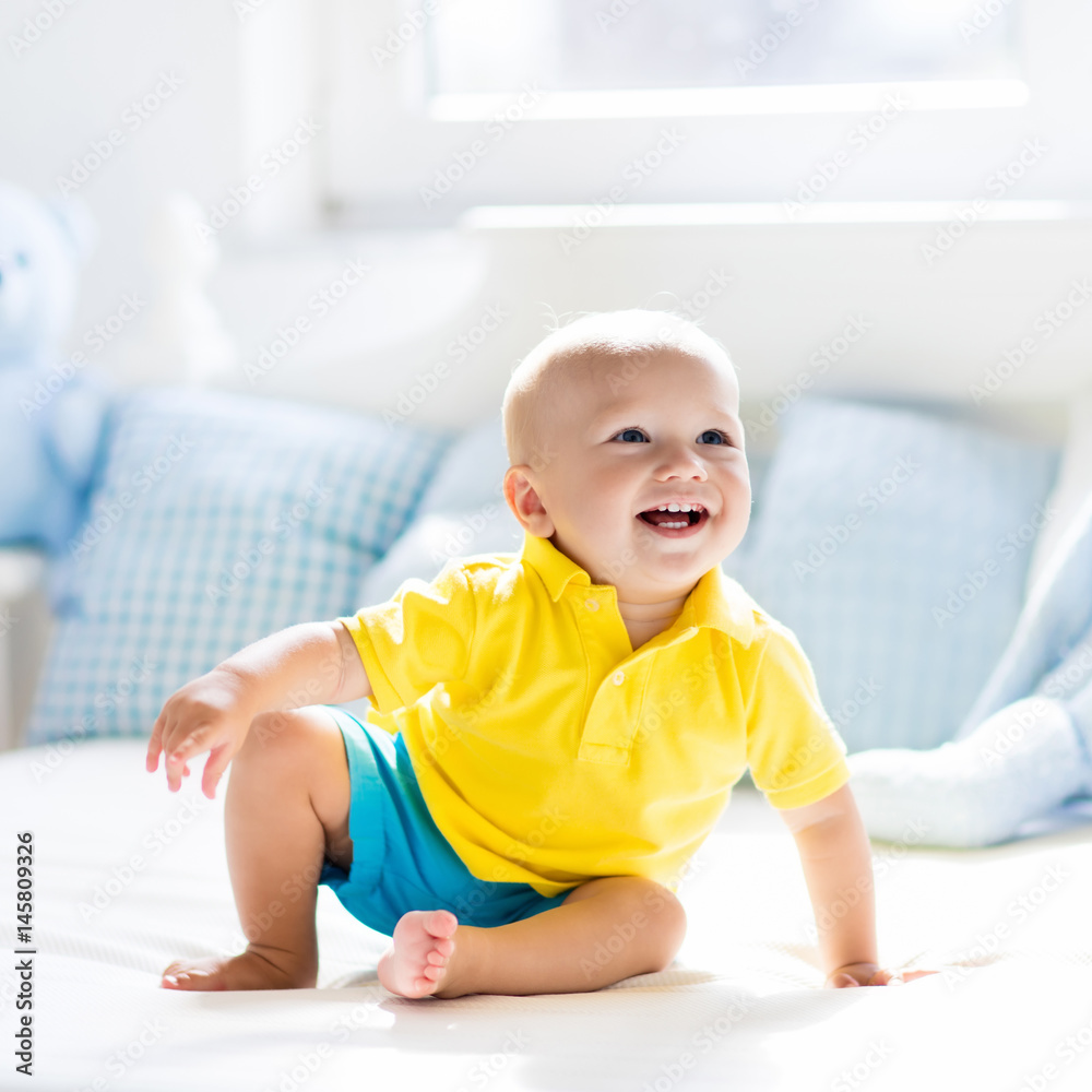 Baby boy playing on bed in sunny nursery Baby boy playing on bed in sunny nursery