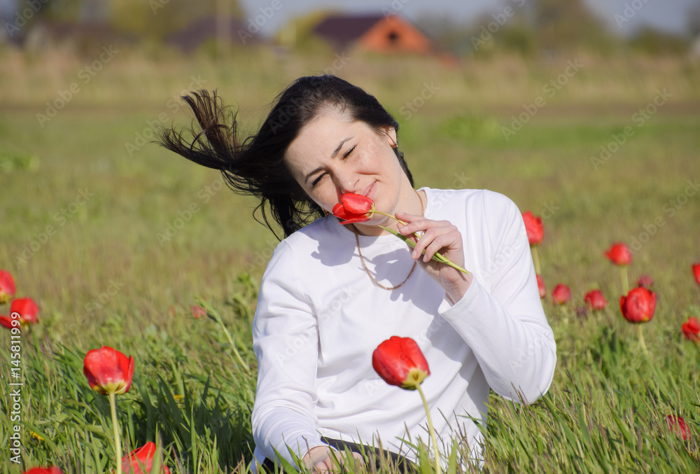 Beautiful fairy young girl in a field among the flowers of tulips. Portrait of a girl on a background of red flowers and a green field. Field of tulips Beautiful fairy young girl in a field among the flowers of tulips. Portrait of a girl on a background of red flowers and a green field. Field of tulips