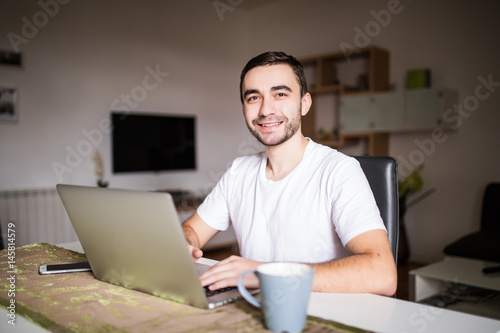 Portrait of young man using laptop while having breakfast in the morning photo