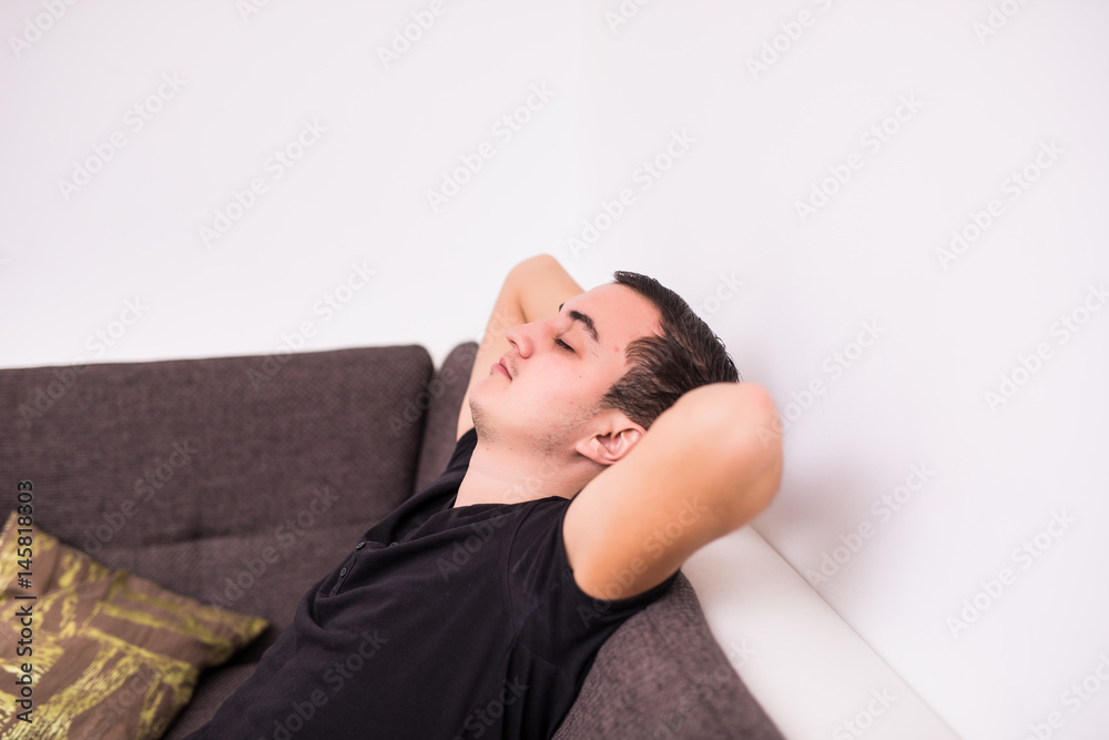 Fototapeta premium Handsome man is looking away while sitting on couch at home