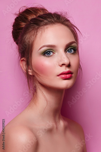 Beautiful young graceful girl with long neck on a pink background in studio. The hair is collected in a high beam. Brown. Fresh bright make-up, green shadows, pink lipstick and blush. Cosmetics.
