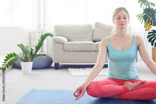 Beautiful chestnut practicing lotus pose on yoga mat indoor