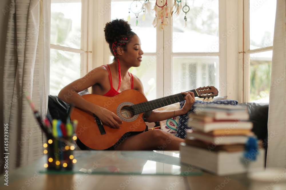 Fototapeta premium Mixed Race Girl Singing And Playing Classic Guitar At Home