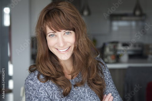 Portrait Of A Mature woman smiling At The Camera. In the kitchen.