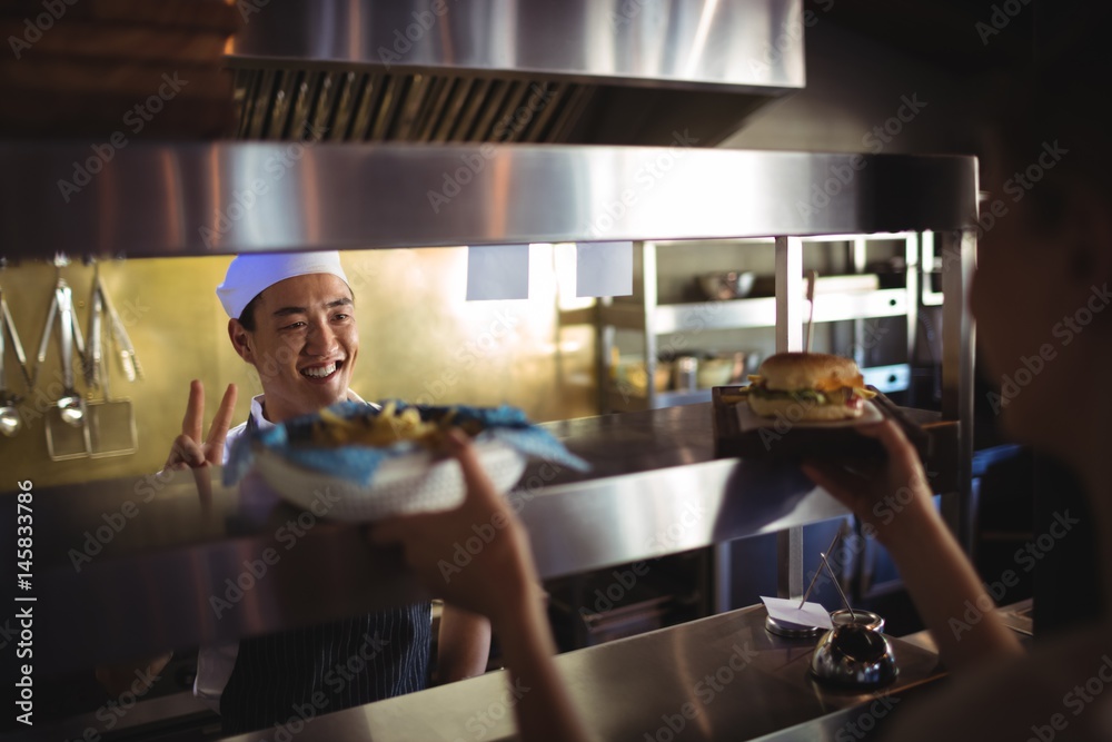 Chef passing tray with french fries and burger to waitress Chef passing tray with french fries and burger to waitress