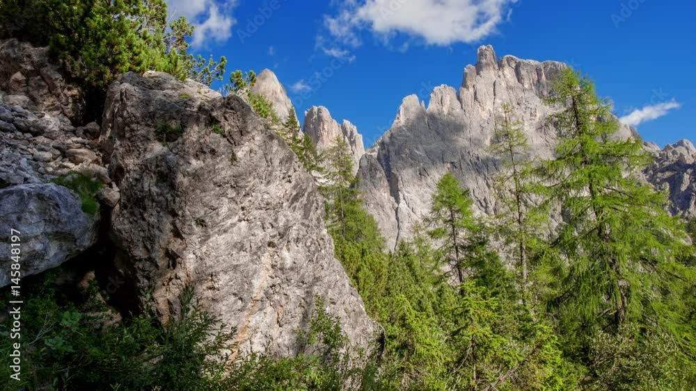 Time-lapse of a rocky mountain peak with puffy clouds  and pine trees.