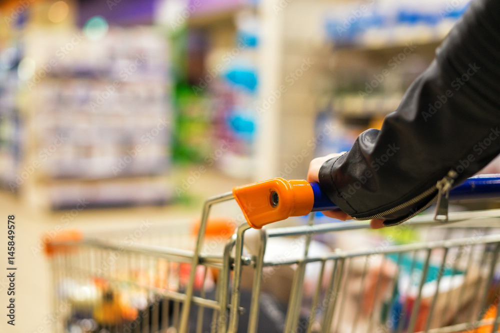 Abstract photo of woman carrying a cart or trolley in the supermarket. Blurred background