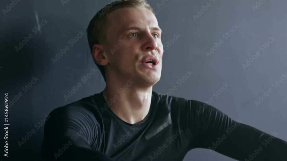 Close up with tilt down of exhausted fighter in boxing gloves sitting on floor of gym and breathing heavily after workout Close up with tilt down of exhausted fighter in boxing gloves sitting on floor of gym and breathing heavily after workout
