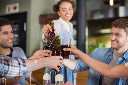 Young friends toasting beer bottles in pub