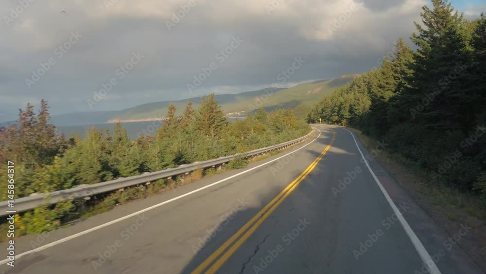 POV CLOSE UP: Traveling on empty coastal highway through Canadian spruce forest towards rocky cliffy coastline in Cape Breton, Nova Scotia. Road trip across Canada along the North Atlantic ocean shore POV CLOSE UP: Traveling on empty coastal highway through Canadian spruce forest towards rocky cliffy coastline in Cape Breton, Nova Scotia. Road trip across Canada along the North Atlantic ocean shore