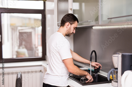 Happy young man standing and washing dishes on the kitchen
