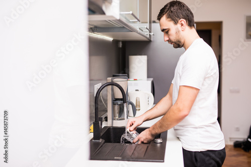 young happy man doing the dishes smiling confident and relaxed enjoying doing domestic work in fun and positive male housework duty