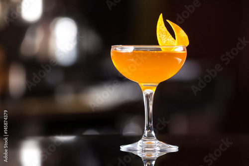 Obraz na płótnie Glass of orange cocktail decorated with lemon at bar counter background