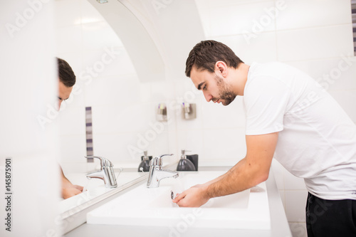 Handsome man washing face in bathroom in morning