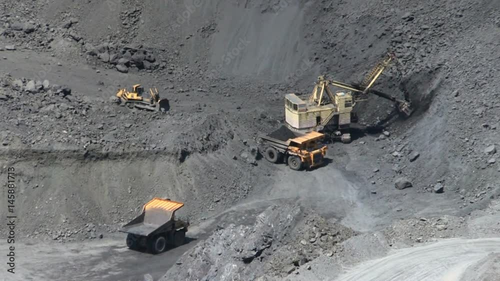 Excavator loading iron ore into the heavy dump truck on the open cast mine. Excavator loading iron ore into the heavy dump truck on the open cast mine.