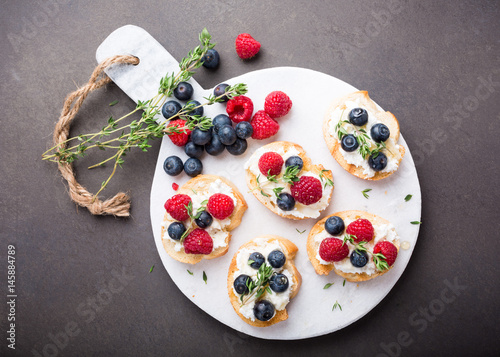 Sandwiches with fresh berries, goat cheese and honey on marble cutting board, top view, copy space.