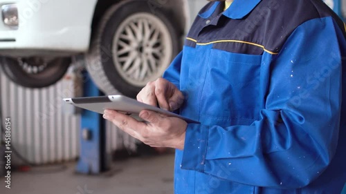 hands of man car mechanic with tablet with lifted car on background photo