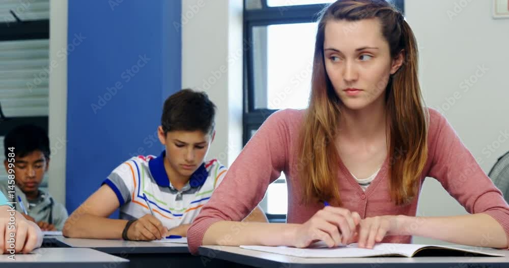 Schoolgirl passing chit to her classmate during exam in classroom Schoolgirl passing chit to her classmate during exam in classroom