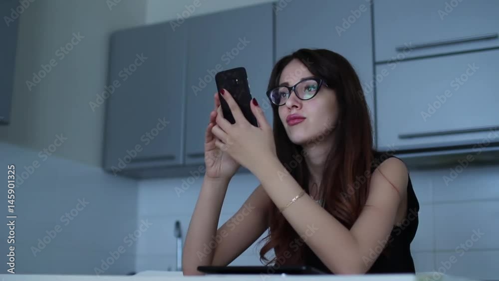 Attractive young woman using her mobile cell phone sitting at kitchen Attractive young woman using her mobile cell phone sitting at kitchen