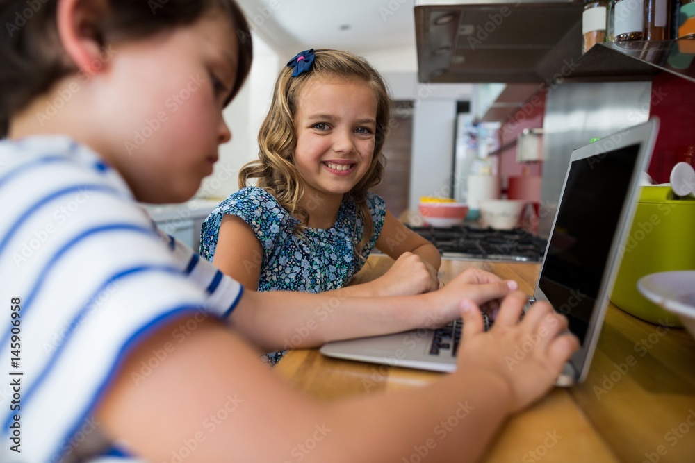 Smiling siblings using laptop in kitchen Smiling siblings using laptop in kitchen