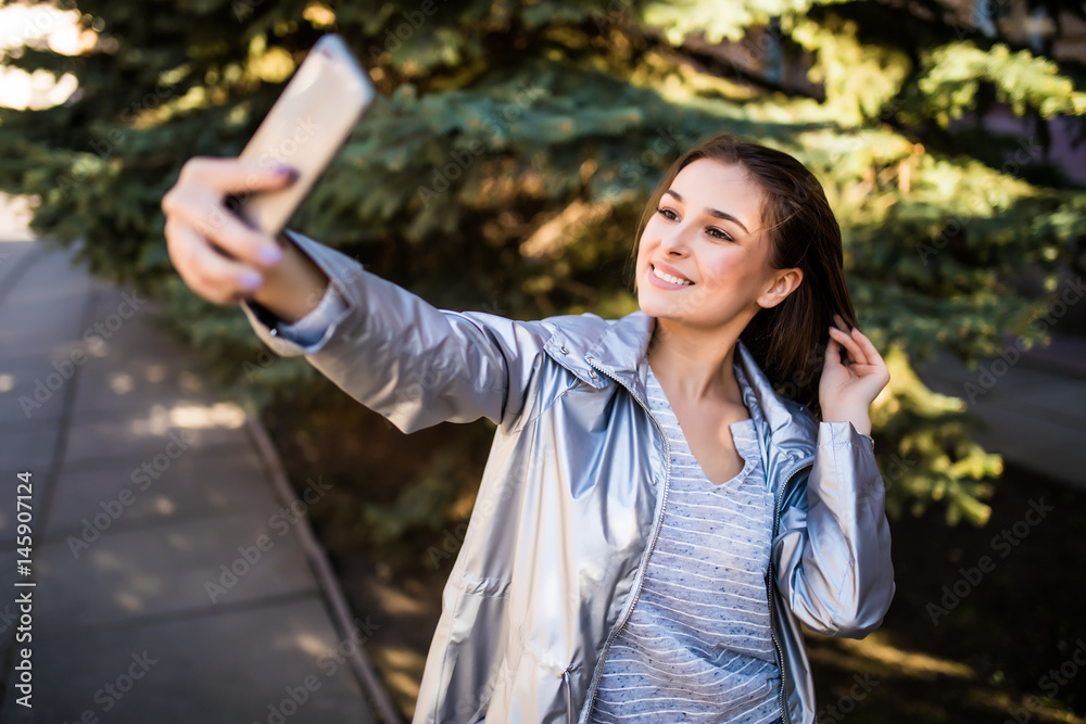 Naklejka premium Young girl take selfie from hands with phone on summer city street. Urban life concept.